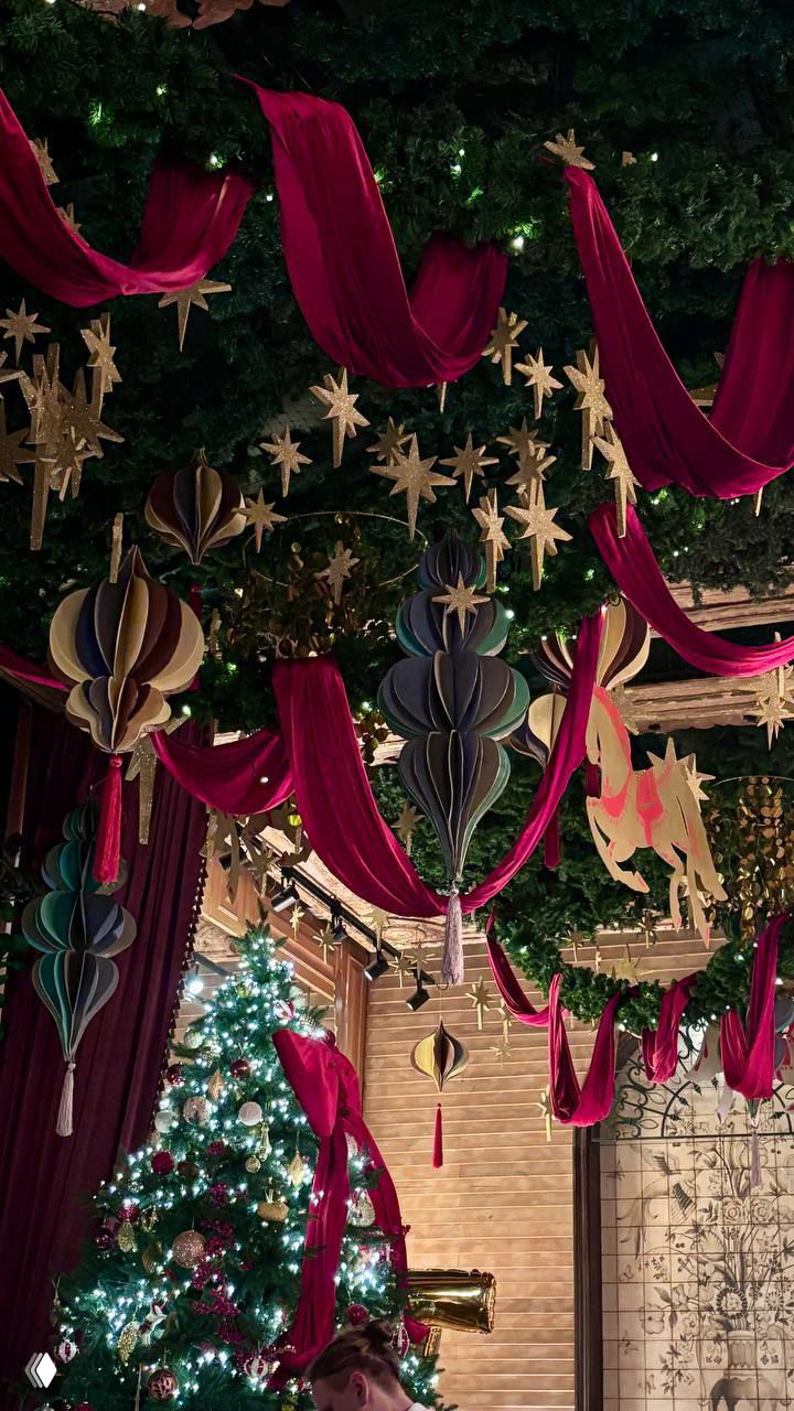 Широкий кадр потолочных украшений и витрины с большой рождественской ёлкой, красные тканевые драпировки усиливают праздничную атмосферу