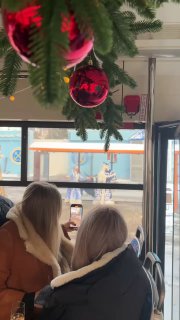 Новогодние украшения в салоне трамвая над головами зрителей; несколько людей снимают происходящее на смартфоны, фиксируя представление.