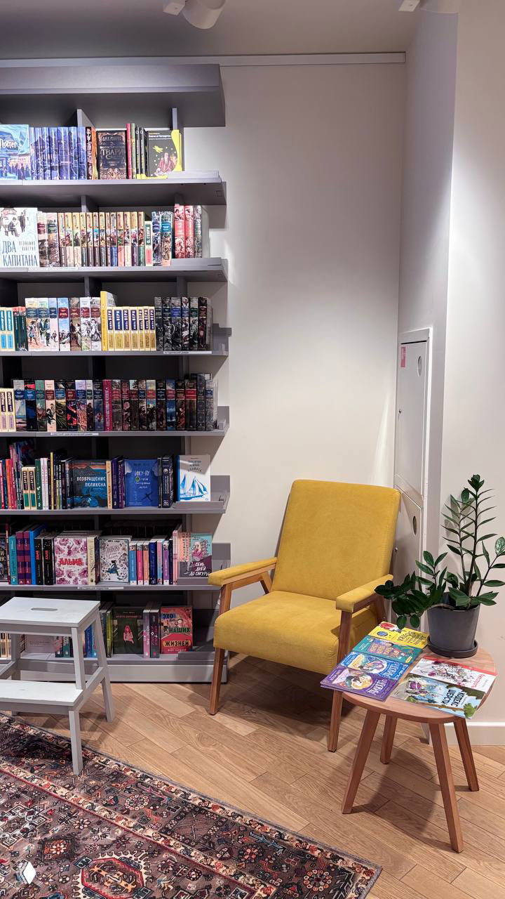 Интерьер книжного Пиотровский: стеллажи с книгами, жёлтое кресло и столик — уютная зона чтения внутри Ельцин центра рядом с экспозицией.