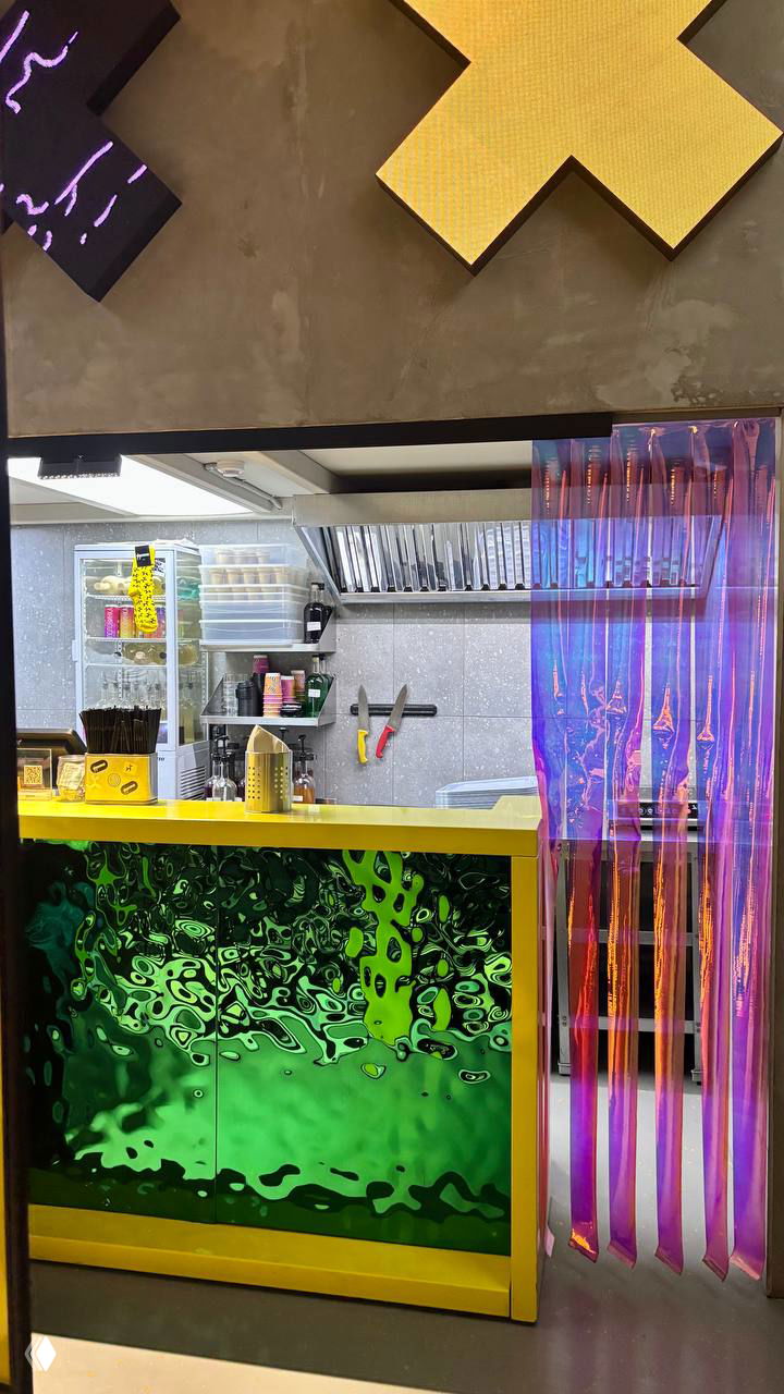 Барная стойка в ярких жёлто-зелёных тонах, вид на кухню и блестящую декоративную занавеску, необычный дизайн помещения.