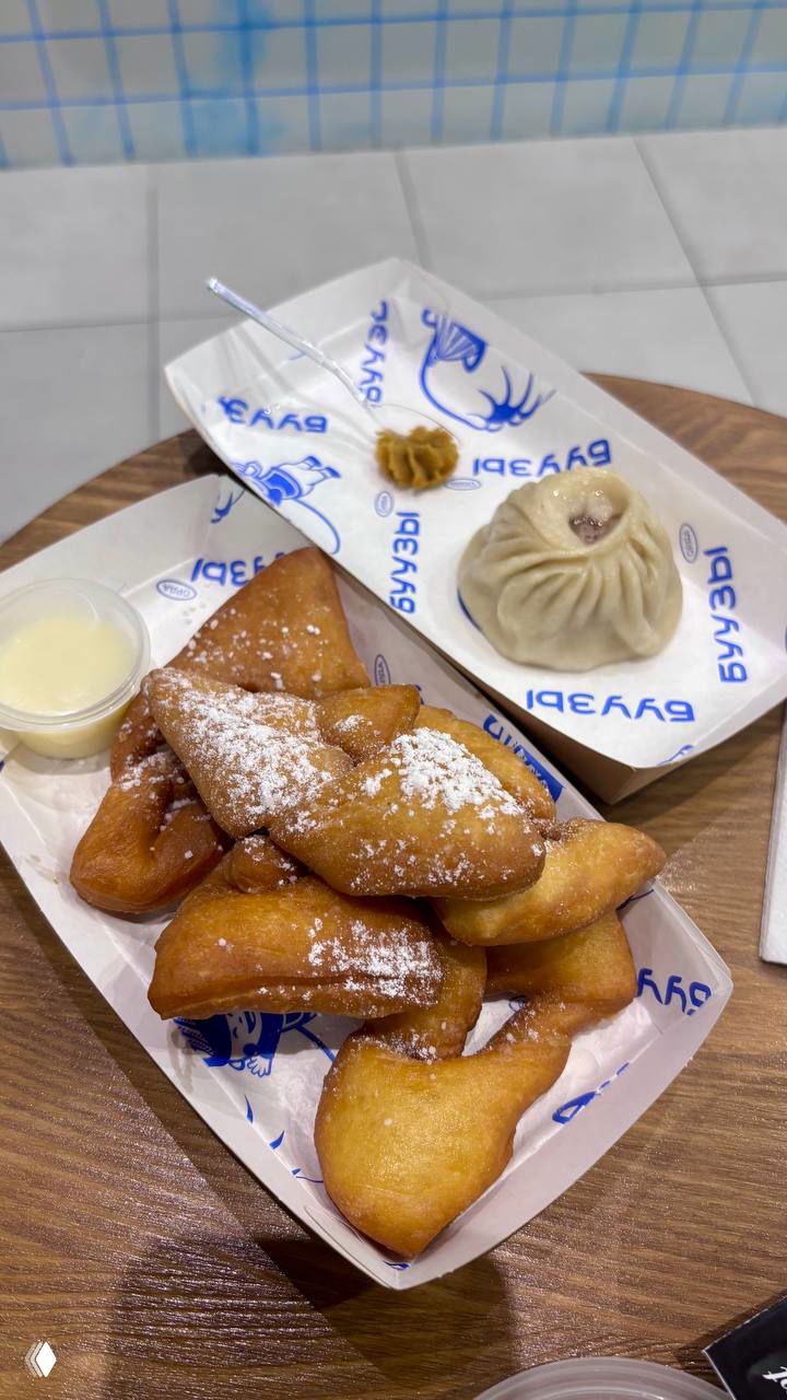 Тарелка с несколькими кусочками хрустящих жареных тестовых изделий и одна паровая бууза, посыпанные сахарной пудрой — десертная подача