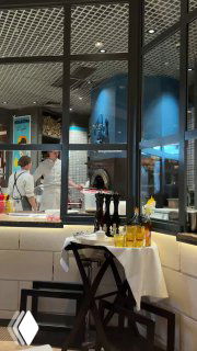 Интерьер La Bottega Siciliana: открытая кухня и печь, повара готовят за стеклом, стол с бутылками масла и сервировкой, вид из зала на рабочую зону.