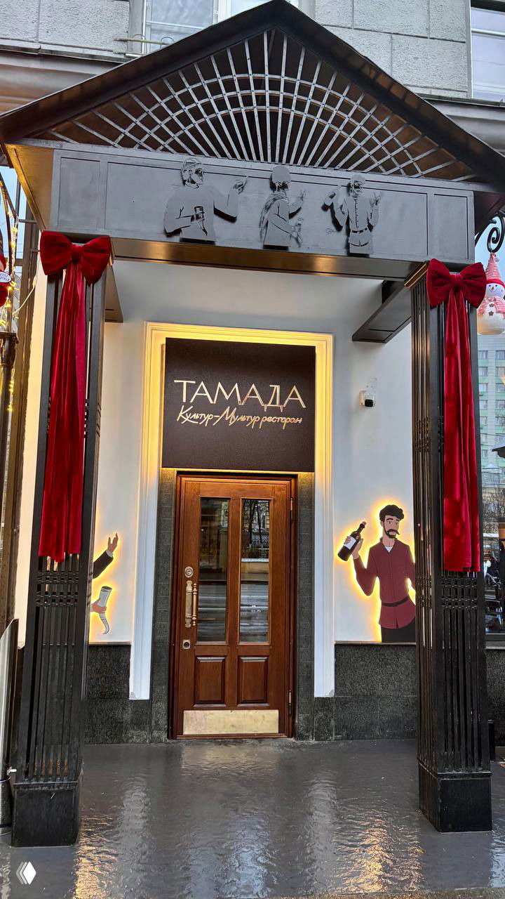 Входная группа ресторана с вывеской «Тамада» и оформлением фасада: дверь в классическом стиле и иллюстрации с вином по бокам.