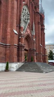 Общий вид фасада готического собора с главным порталом, розеткой и острыми шпилями на фоне пасмурного неба, архитектурная перспектива.