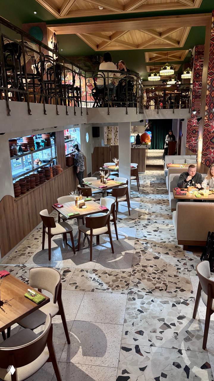 Общий вид двухуровневого зала ресторана с расстановкой столов, тканевыми салфетками и декоративными элементами на стенах, тёплое освещение.