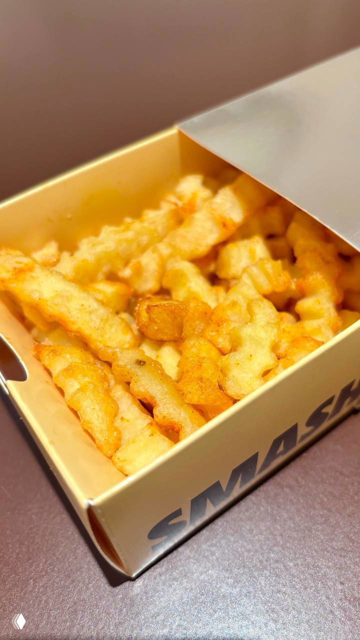 Коробка картофеля фри крупным планом: фигурный картофель в бежевой коробочке с логотипом, аппетитный золотистый оттенок и текстура.