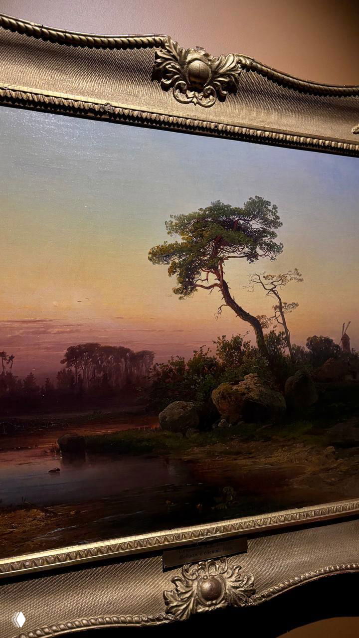 Крупный фрагмент живописного пейзажа в декоративной позолоченной раме; виднеются камни, хвойное дерево и тёплый закатный свет на полотне.