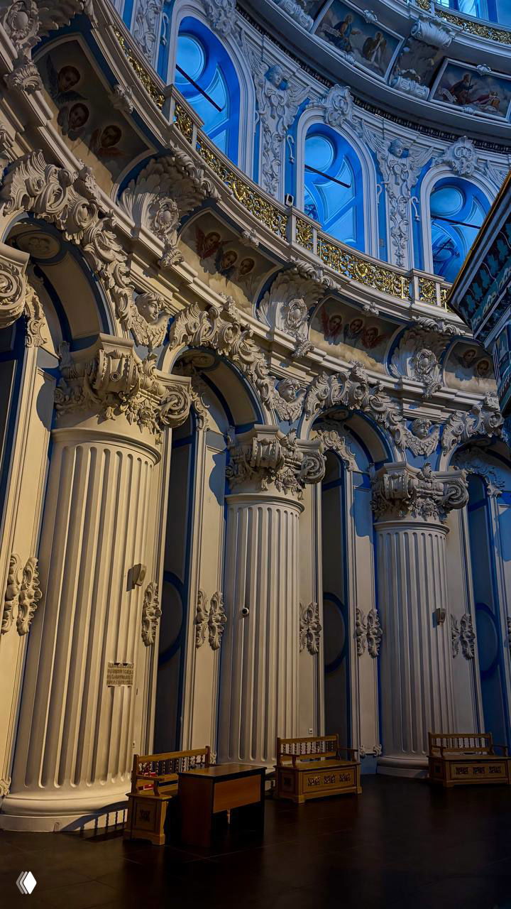 Фрагмент интерьера с декоративными колоннами и балконами: барочная отделка, золочёные элементы и повторяющаяся орнаментальная структура.