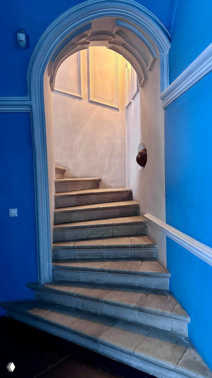 Узкая лестница внутри монастырского здания: каменные ступени, арочный проём и мягкий вечерний свет, ведущие на верхние уровни комплекса.