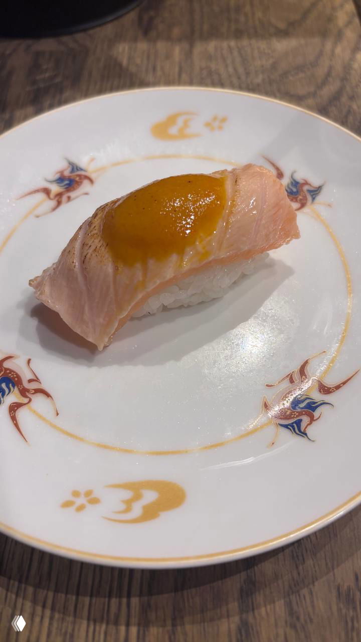 Нигири с опалённым лососем: кусочек рыбы на рисе с насыщенным соусом сверху, поданное на тонкой фарфоровой тарелке.