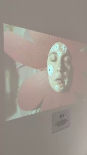 Кадр видео-проекции с картонной ромашкой и крупным планом маски/лица — часть инсталляции в галерее Culture.