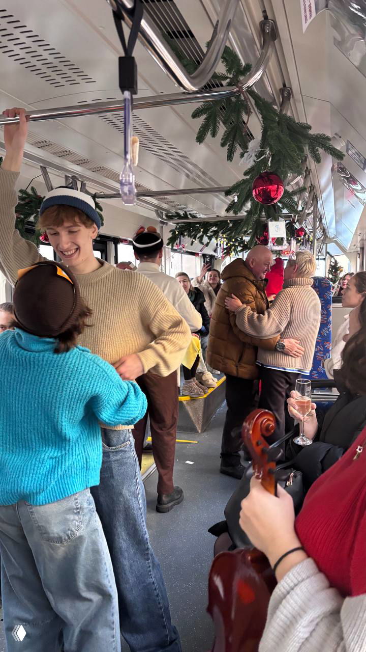 Широкий кадр салона трамвая с музыкальными инструментами, танцующими парами и гирляндами на потолке; праздничный общий план мероприятия.