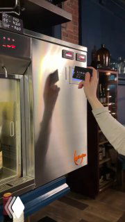 Рука сотрудника нажимает на панель эноматика в металлическом корпусе — процесс выбора и отбора порции вина картой или кнопкой в ресторане.