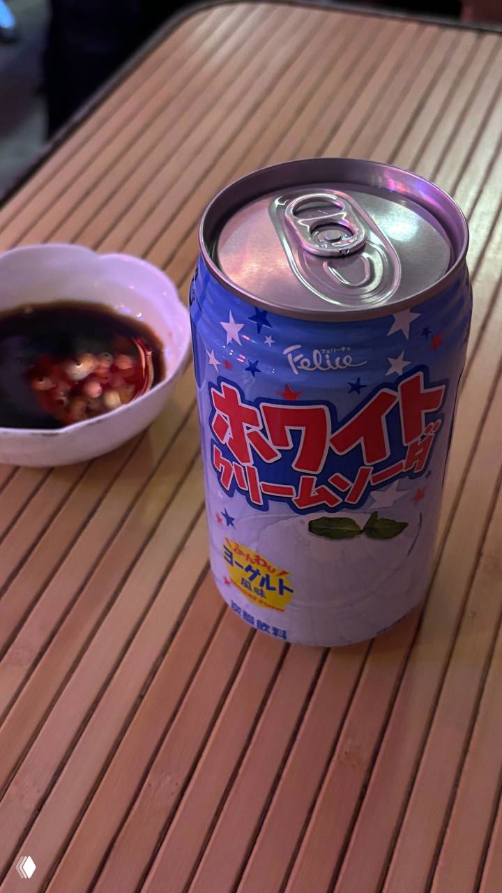 Баночка японской газировки на деревянном столе рядом со соевым соусом и чили — деталь столика во время посещения суши-ресторана.