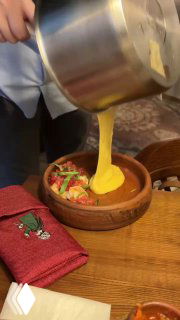 Официант в процессе наливания тягучего сыра прямо в тарелку с ингредиентами — демонстрация фондю в авторском стиле заведения.