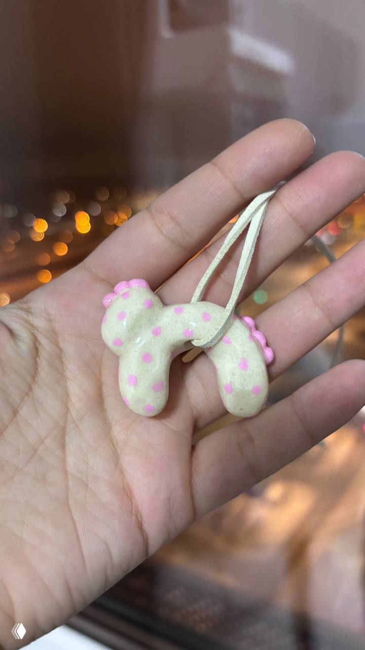 Милая лошадка-шарм из теста на шнурке в руке автора на фоне праздничной гирлянды — подарок пекарни в рамках новогоднего проекта.