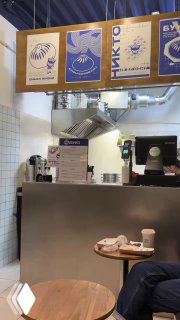 Интерьер маленького семейного фастфуда: прилавок, касса и открытая кухня за которой работают повара, столики на переднем плане