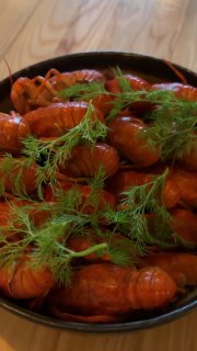 Крупный вертикальный кадр с тарелкой варёных раков и зеленью на столе в ресторане — детали подачи и текстуры панировки и укропа.