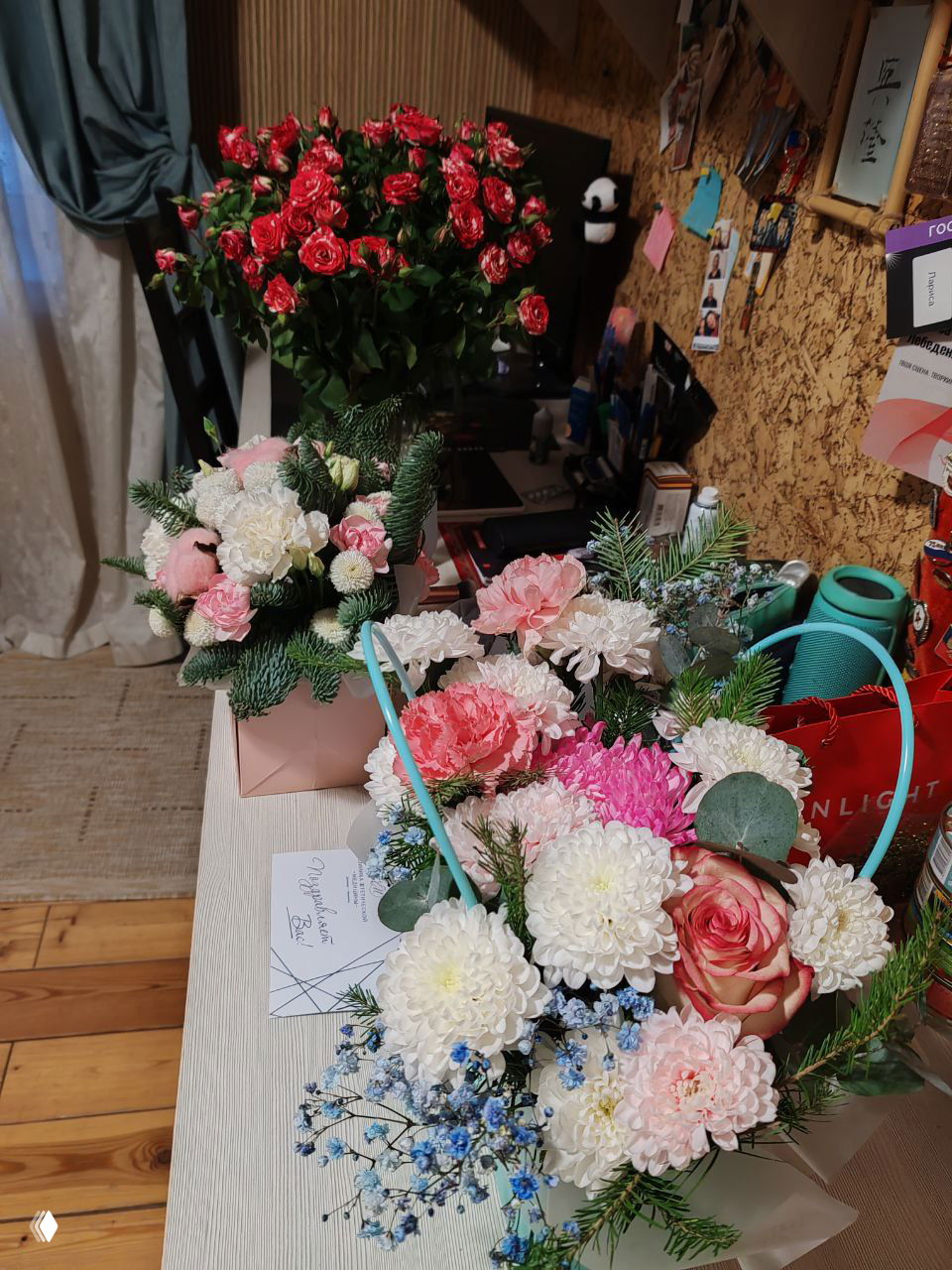 Букеты и цветочные композиции на столе в домашнем интерьере: белые и розовые хризантемы, розы, зелень и поздравительные открытки.