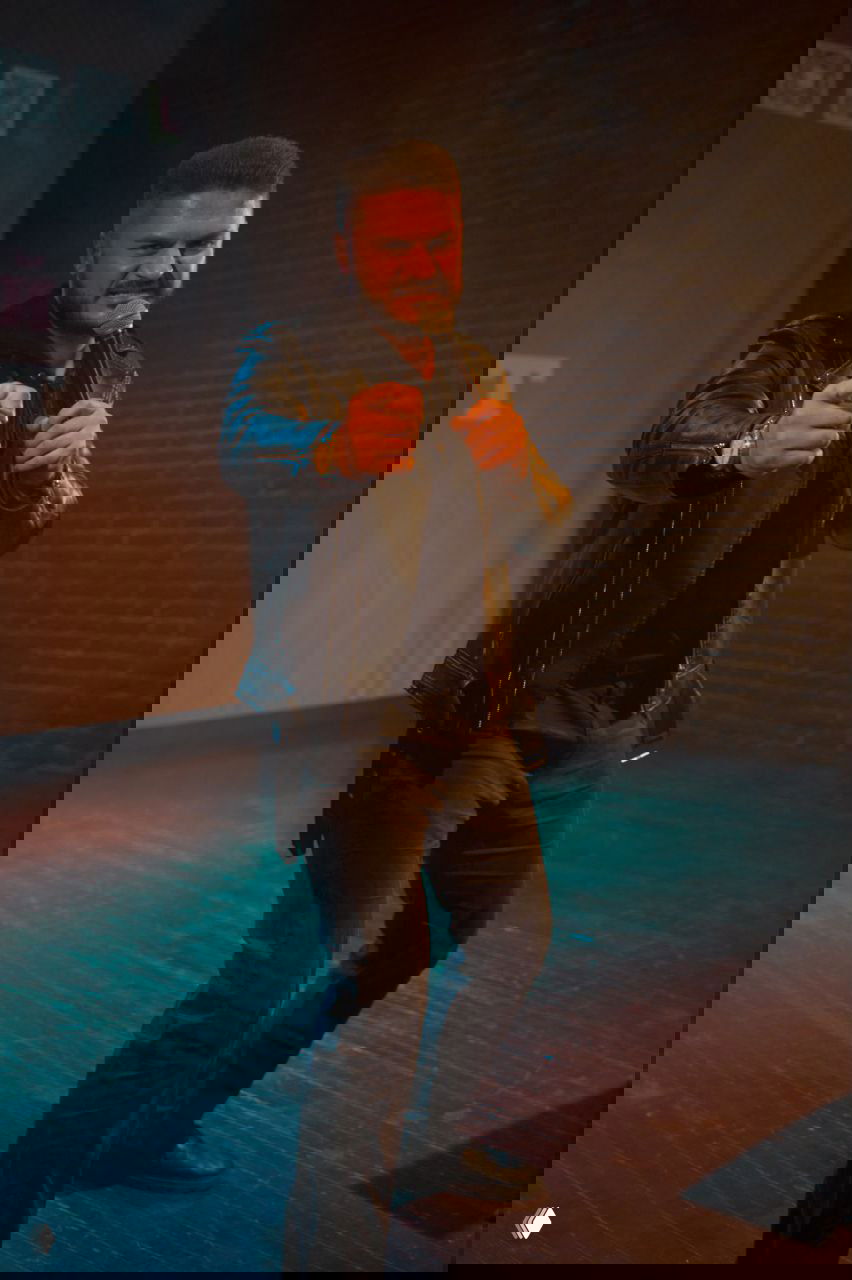 Певец в чёрной кожаной куртке у микрофона, энергичный жест в сторону зрителя на тёмной сцене с контрастным освещением