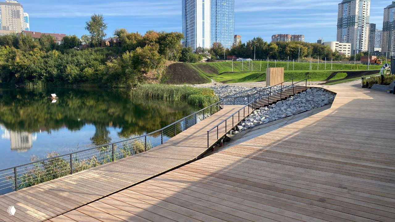 Набережная и деревянная прогулочная зона рядом с озером: реальная фотография прогулочной инфраструктуры и вида на близлежащие дома и зелень.
