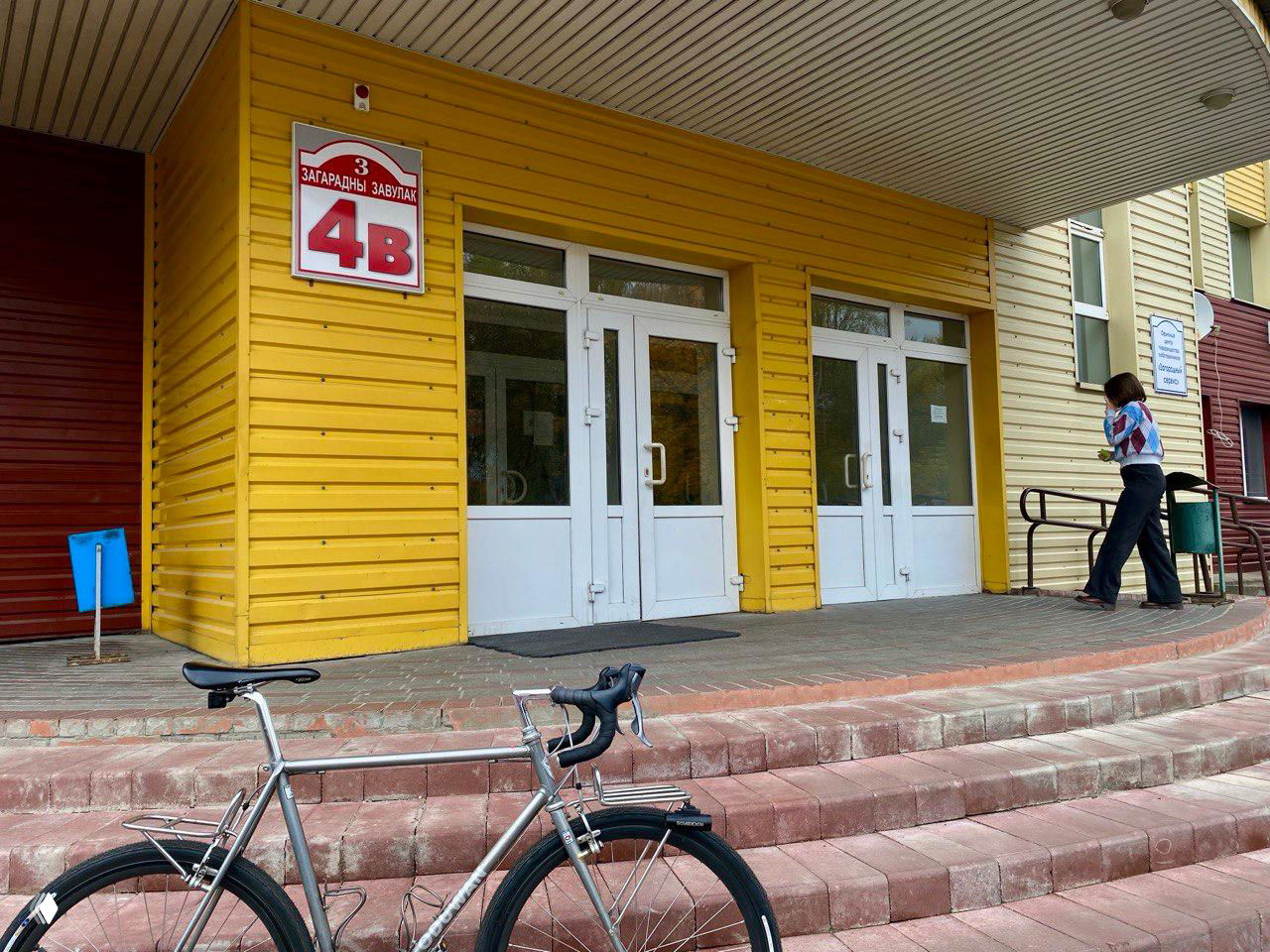 Парадный вход жёлтого здания с номером квартиры/офиса и припаркованным велосипедом на переднем плане; городской фасад и подъезд.