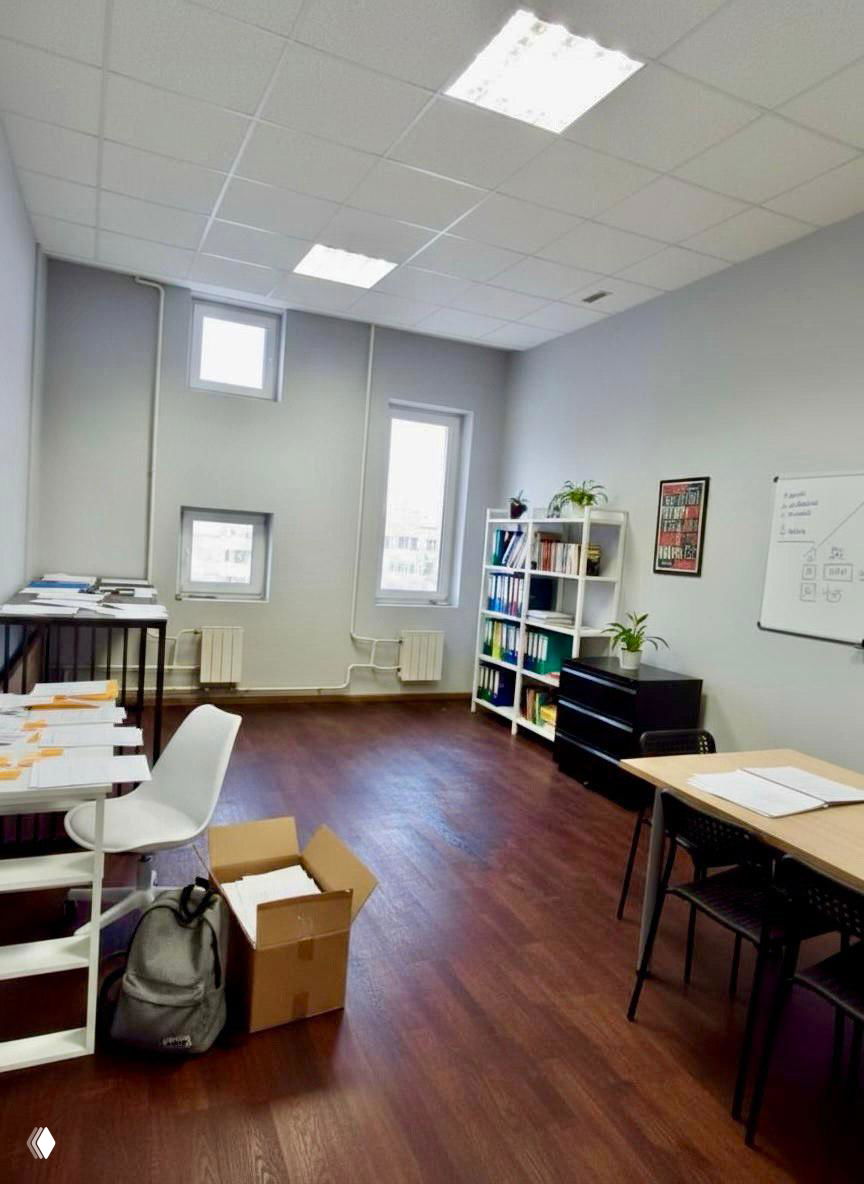 Свободная светлая комната офиса с полками, файлами и столами; организованное рабочее пространство для обработки заказов и документов.