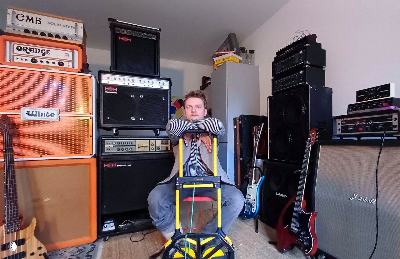 Мужчина сидит в комнате с музыкальным оборудованием: усилители, колонки и электрогитары — пример товаров для выкупа.