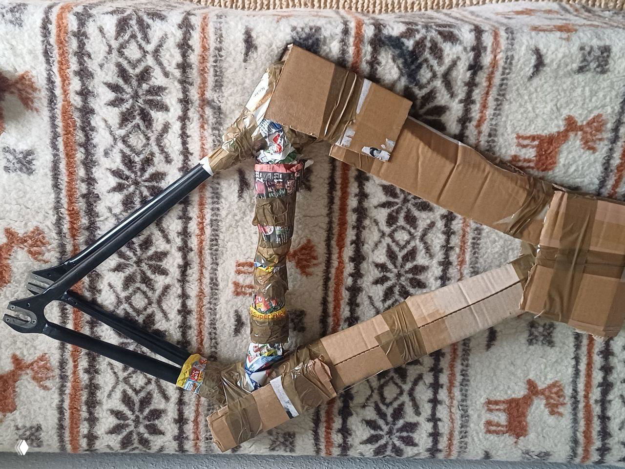 Части велосипедной рамы и труба обмотаны картоном и скотчем; пример самодельной защиты при транспортировке велосипеда в посылке.