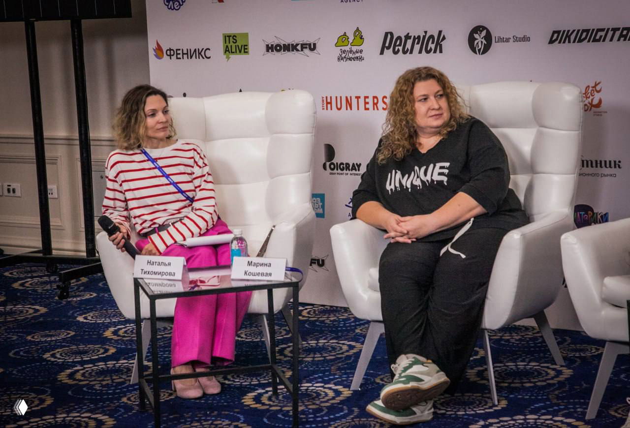 Панельная дискуссия: две участницы сидят в креслах на сцене, рядом столик с табличками и бутылками воды; формат Q&A.