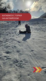 Вертикальное превью: ребёнок на снежной горке сидит внизу склона, солнечный свет, тени и отпечатки на снегу; иллюстрация словаря фраз для катания.