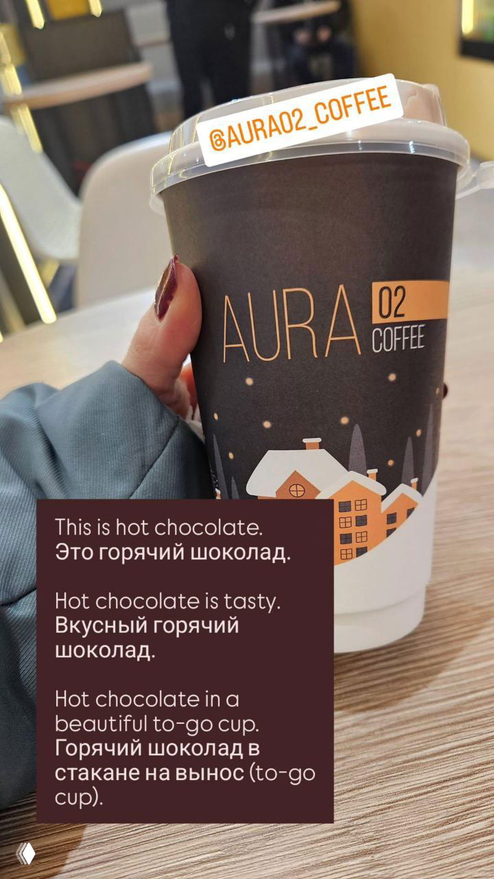 Рука держит бумажный стакан с логотипом AURA 02 Coffee: горячий шоколад в красивом стаканчике на вынос, видна наклейка @AURA02_COFFEE.
