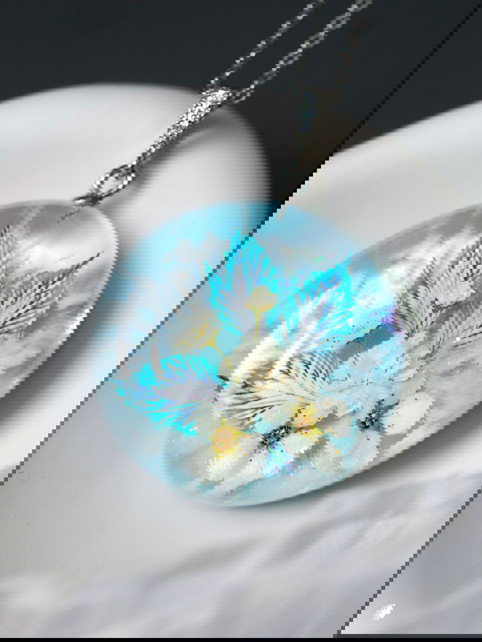 Крупный кулон с натуральными белыми соцветиями и золотыми травами, внутри прозрачной заливки напоминает зимний ландшафт со снежным основанием.