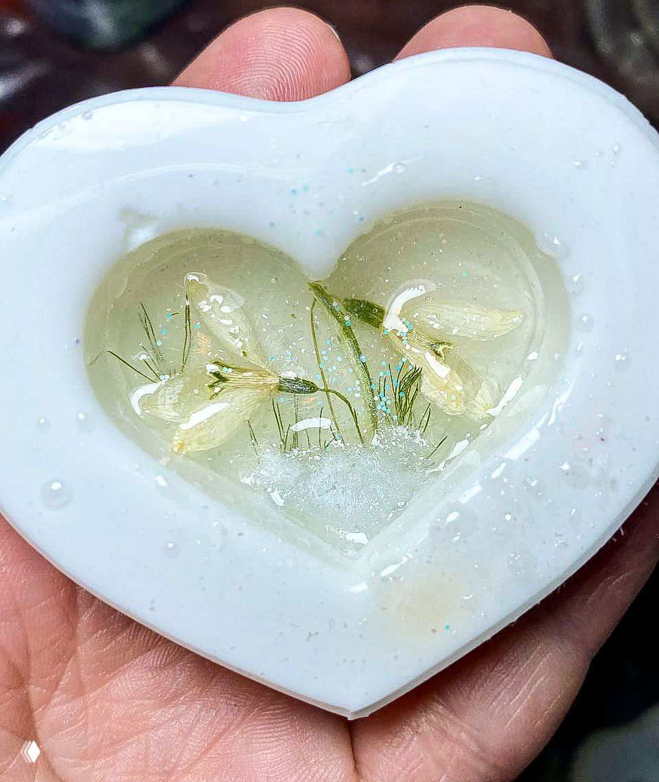 Сердечная силиконовая форма с застывшей в смоле мини‑композицией белых цветков и блёсток — рабочая заготовка ученицы.