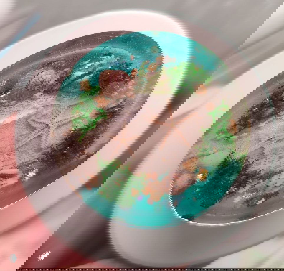 Морская миниатюра в круглой форме: звёздочки, ракушки и зелёные фрагменты под голубой эпоксидной заливкой — эффект пляжа.