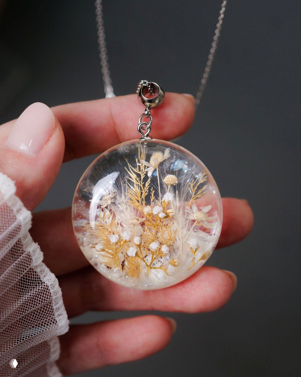Крупный план круглого кулона из прозрачной смолы с миниатюрными засушенными травами, пушистым «снегом» и деликатным мерцанием внутри.