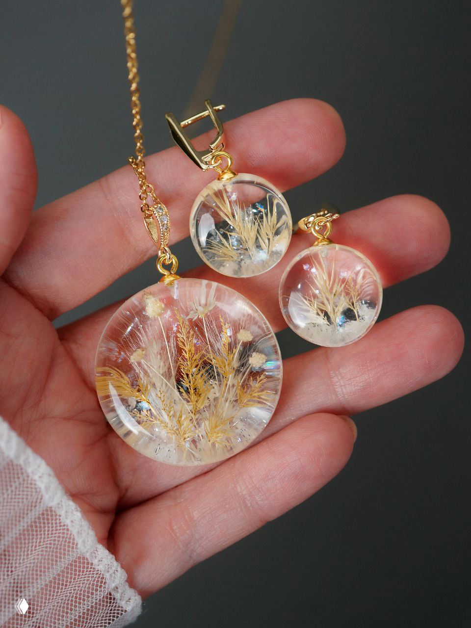 Круглый кулон с мелкими белыми гортензиями, радужными бликами и текстурой внутри прозрачной смолы, показан крупным планом в руке автора.