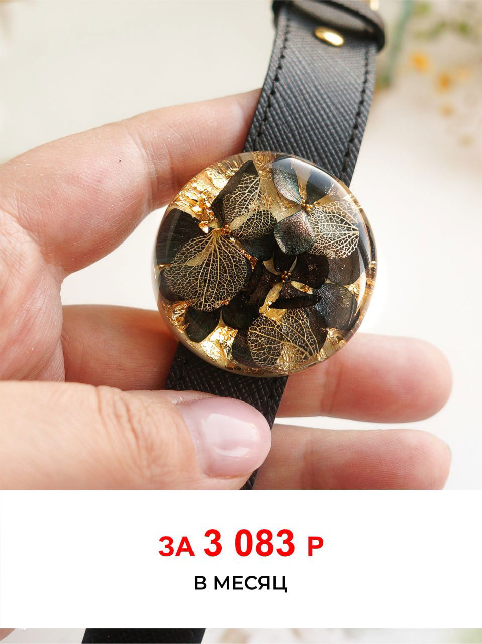 Рука держит круглое украшение из смолы с золотистыми и темными засушенными лепестками и вкраплениями фольги, крупный план для показа деталей техники.