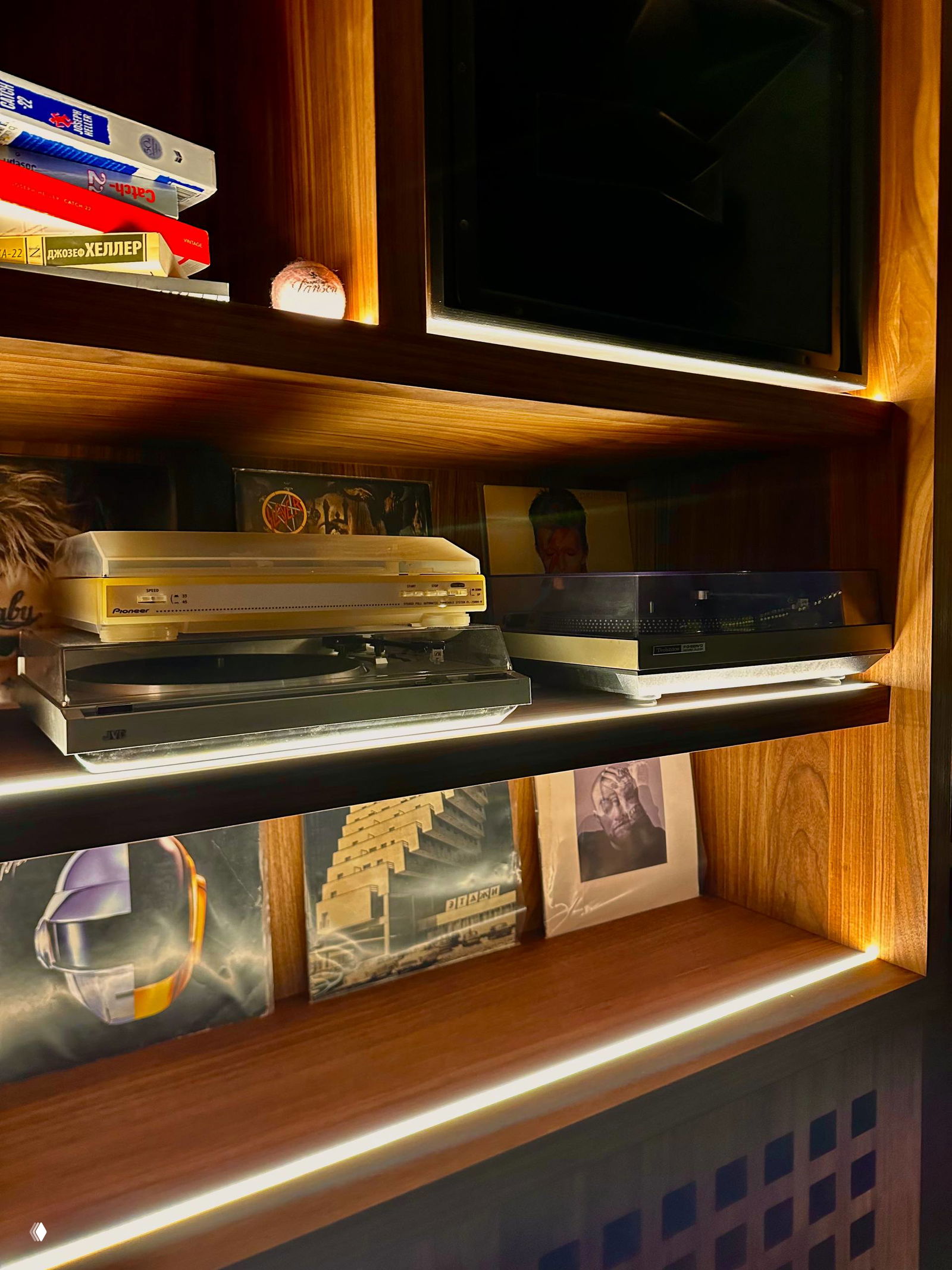Полка с проигрывателями винила и пластинками в деревянной нише бара — видны два проигрывателя и коллекция винила, подчёркнутая подсветкой