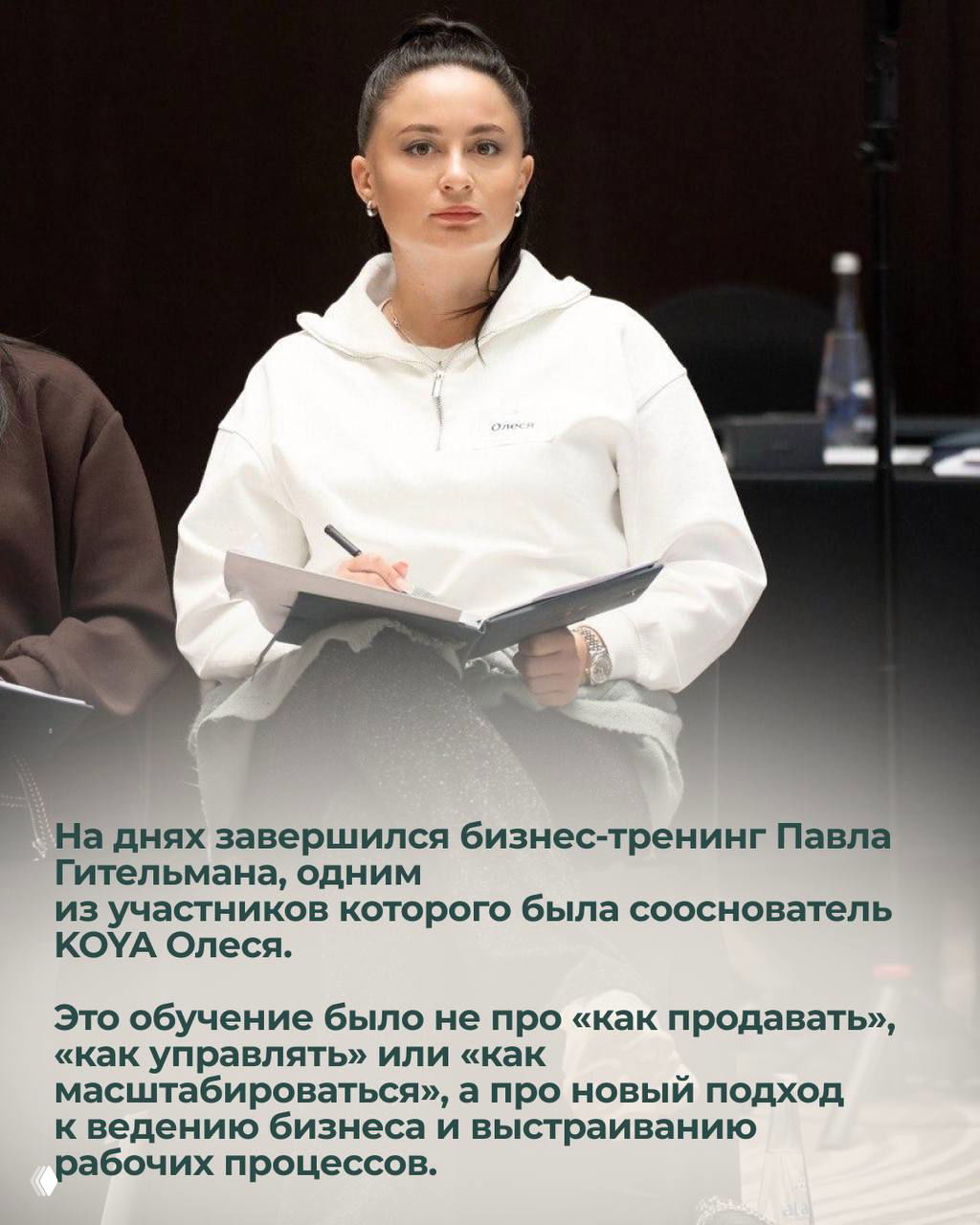 Женщина в светлом худи с блокнотом и ручкой, внимательно слушает и делает заметки во время бизнес-тренинга в конференц-зале.