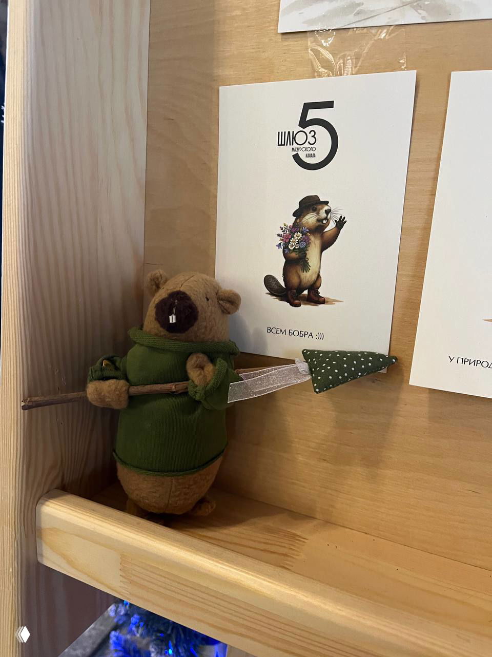 Мягкая игрушка-бобр на деревянной полке рядом с табличкой «Шлюз 5» и маленьким флажком — интерьер кафе или сувенирного уголка.