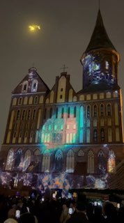 Ночной кадр Кафедрального собора в Калининграде — фасад с праздничным мэппингом и лазерными проекциями; зрители снимают шоу.