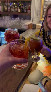 Гости поднимают бокалы и чокаются за барной стойкой: тёплая дружеская атмосфера встречи друзей в Onegin Bar в вечернее время.