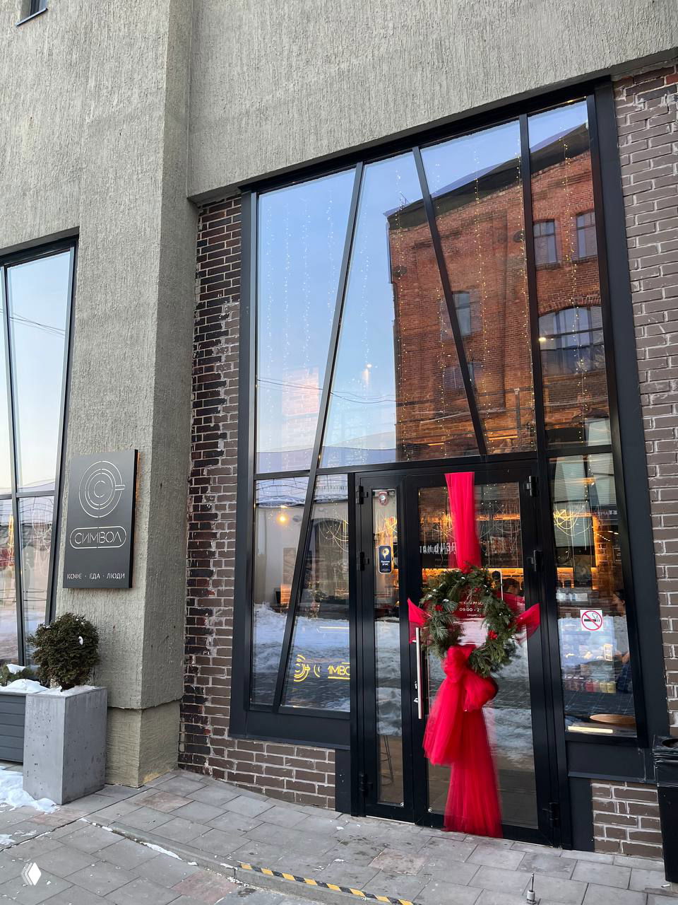 Фасад и вход в кофейню «Символ» на Понарт: стеклянная дверь украшена рождественским венком и красной лентой, виден кирпичный фасад.
