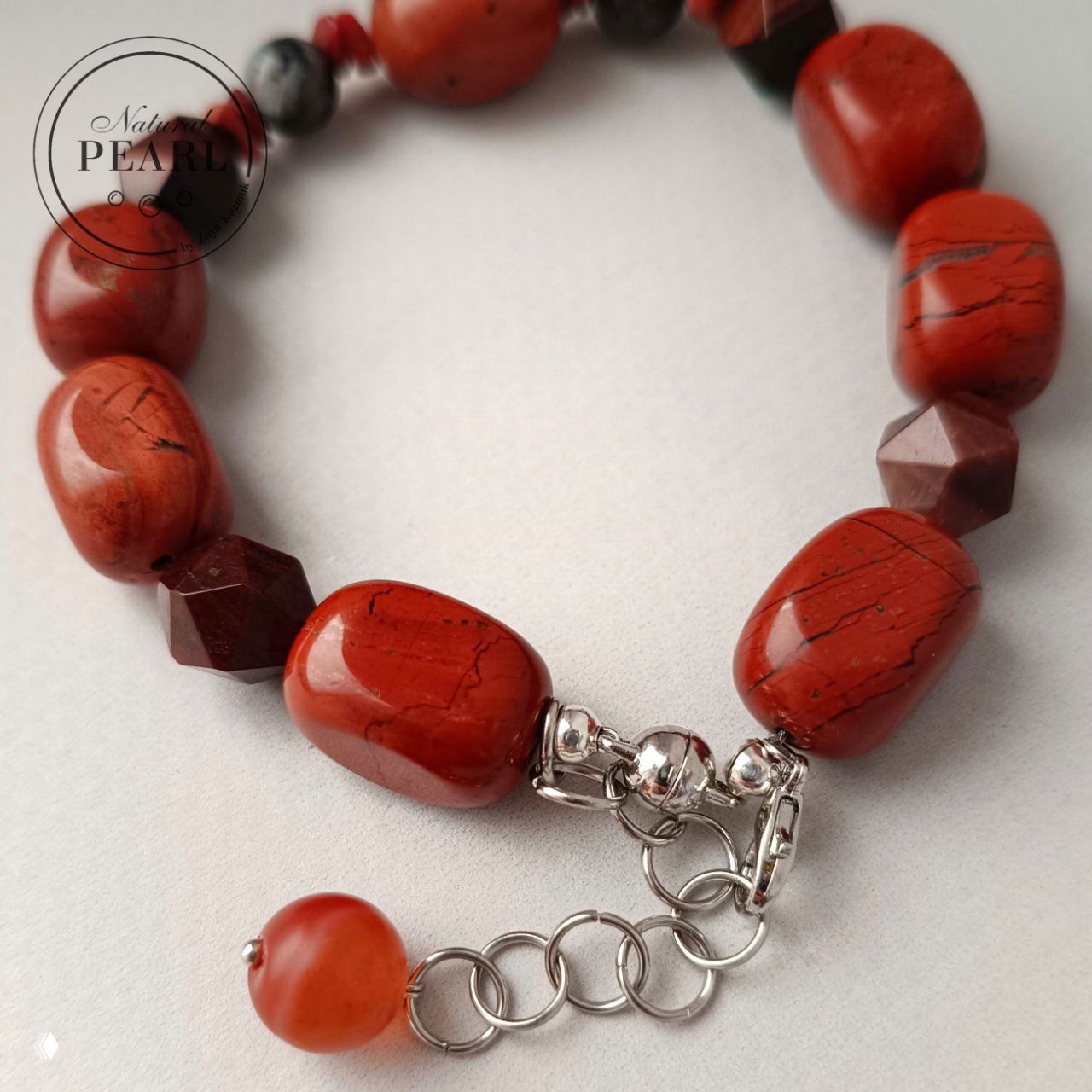 Крупный план застёжки и страховочной цепочки мужского браслета: металлический удлинитель, кольца и завершающая коралловая бусина на цепочке.