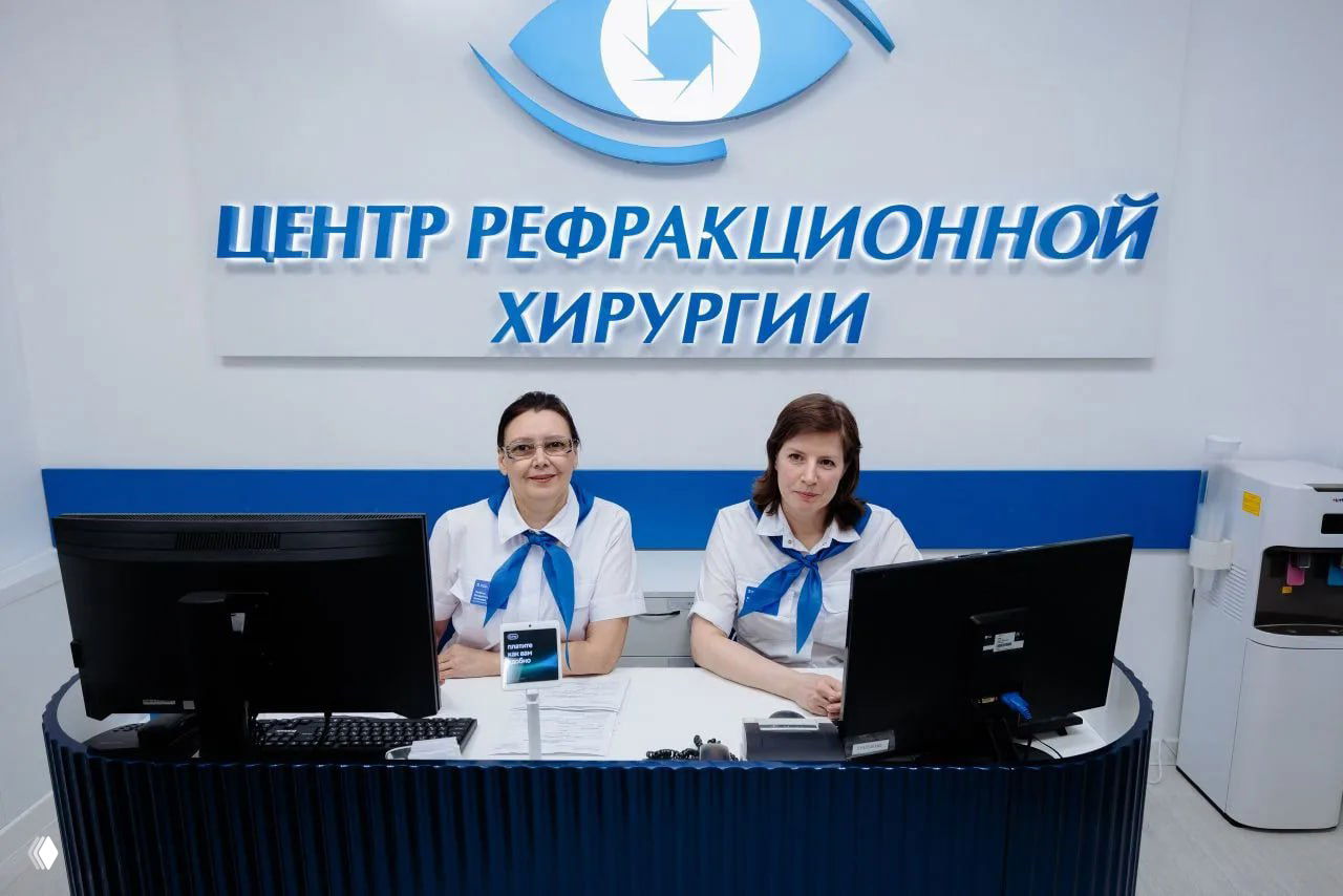 Администраторы в белых блузах и синих галстуках за регистрационной стойкой на фоне вывески «Центр рефракционной хирургии».