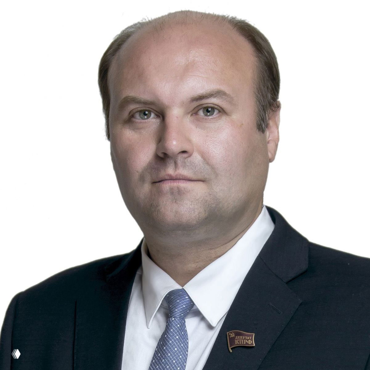 Портретное фото Дениса Сергеевича Сидорова в деловом костюме и галстуке, с нагрудным значком КПРФ на светлом нейтральном фоне, официальный снимок.