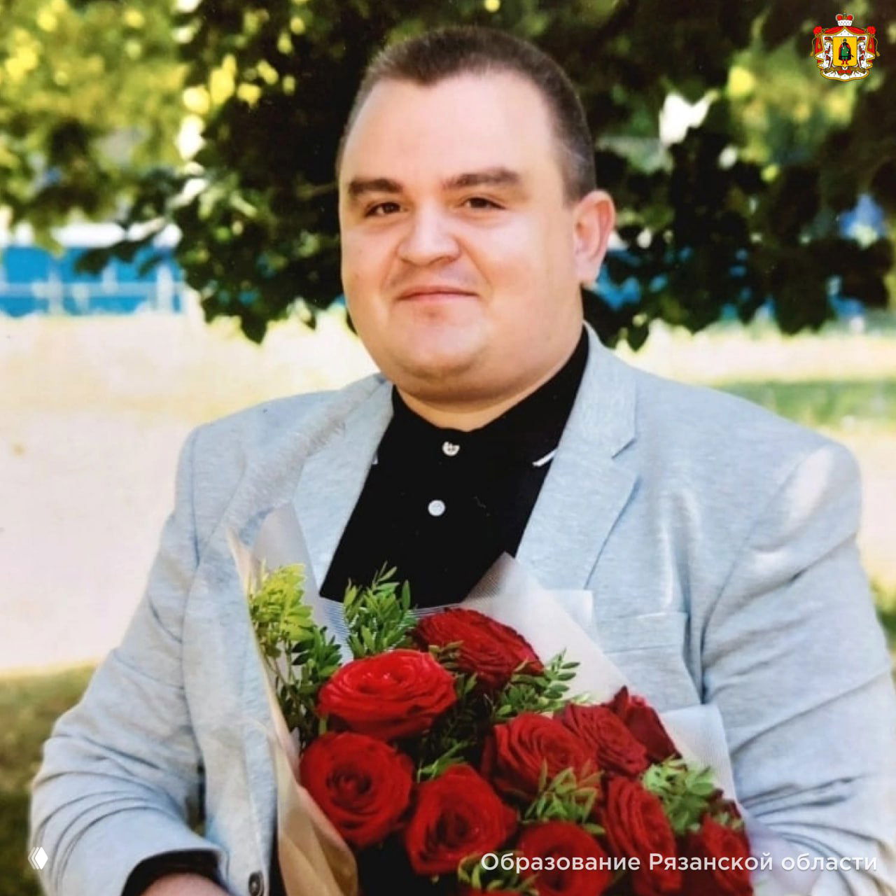 Портрет Александра Кузнецова, учителя информатики из Сасово, в светлом пиджаке держит букет красных роз на улице.