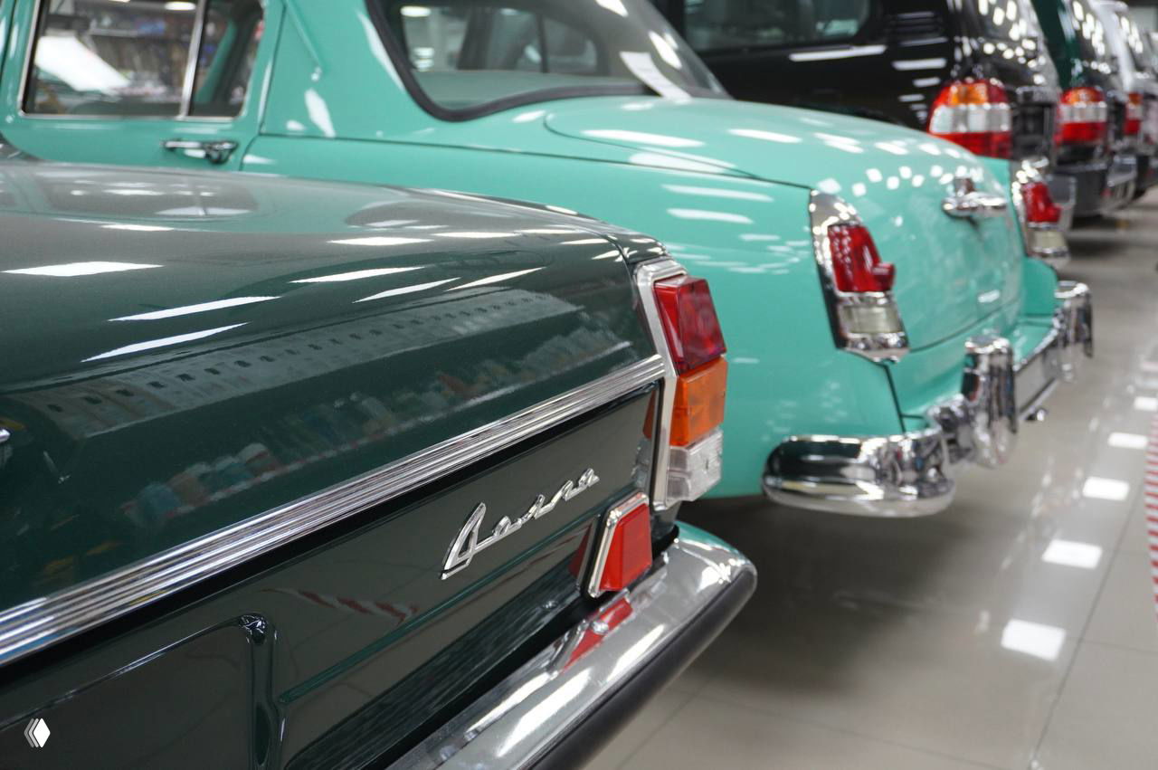 Крупный план задних бамперов и эмблем ретро «Волг» в зелёном и бирюзовом цвете — хромированные детали, надписи модели и аккуратный салон на выставке в Рязани.