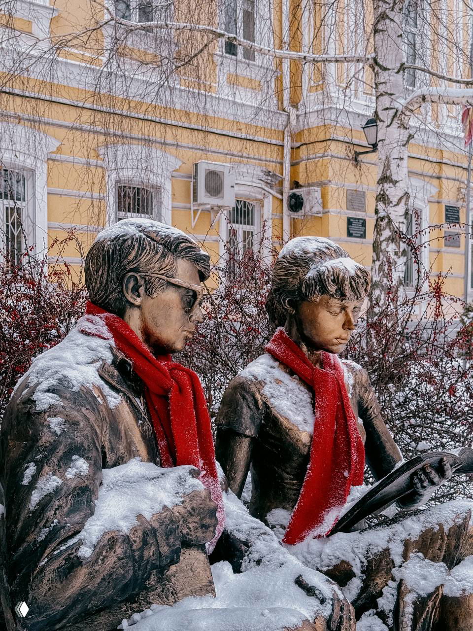Бронзовые скульптуры Шурика и Лидочки в красных шарфах на снегу во дворе РГУ имени Есенина; на заднем плане корпус университета.